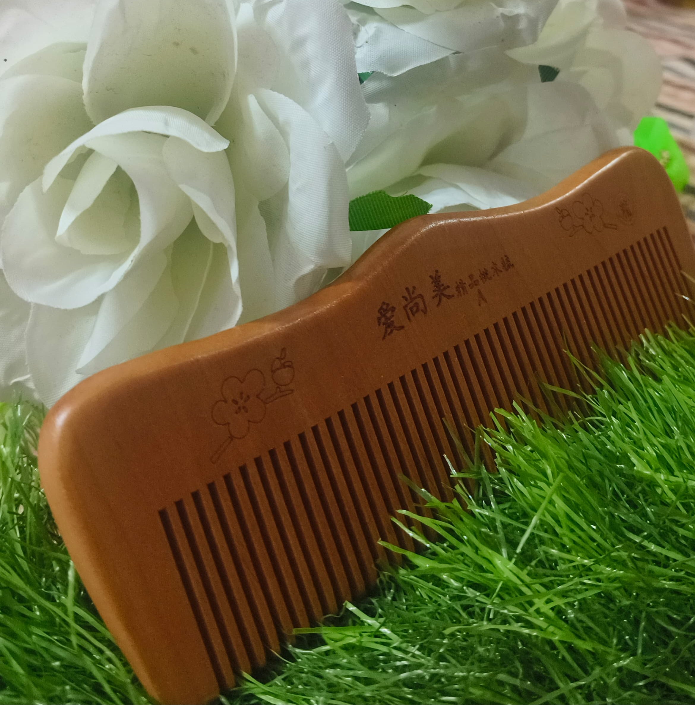 White flowers with a wooden comb on a green surface against a red background